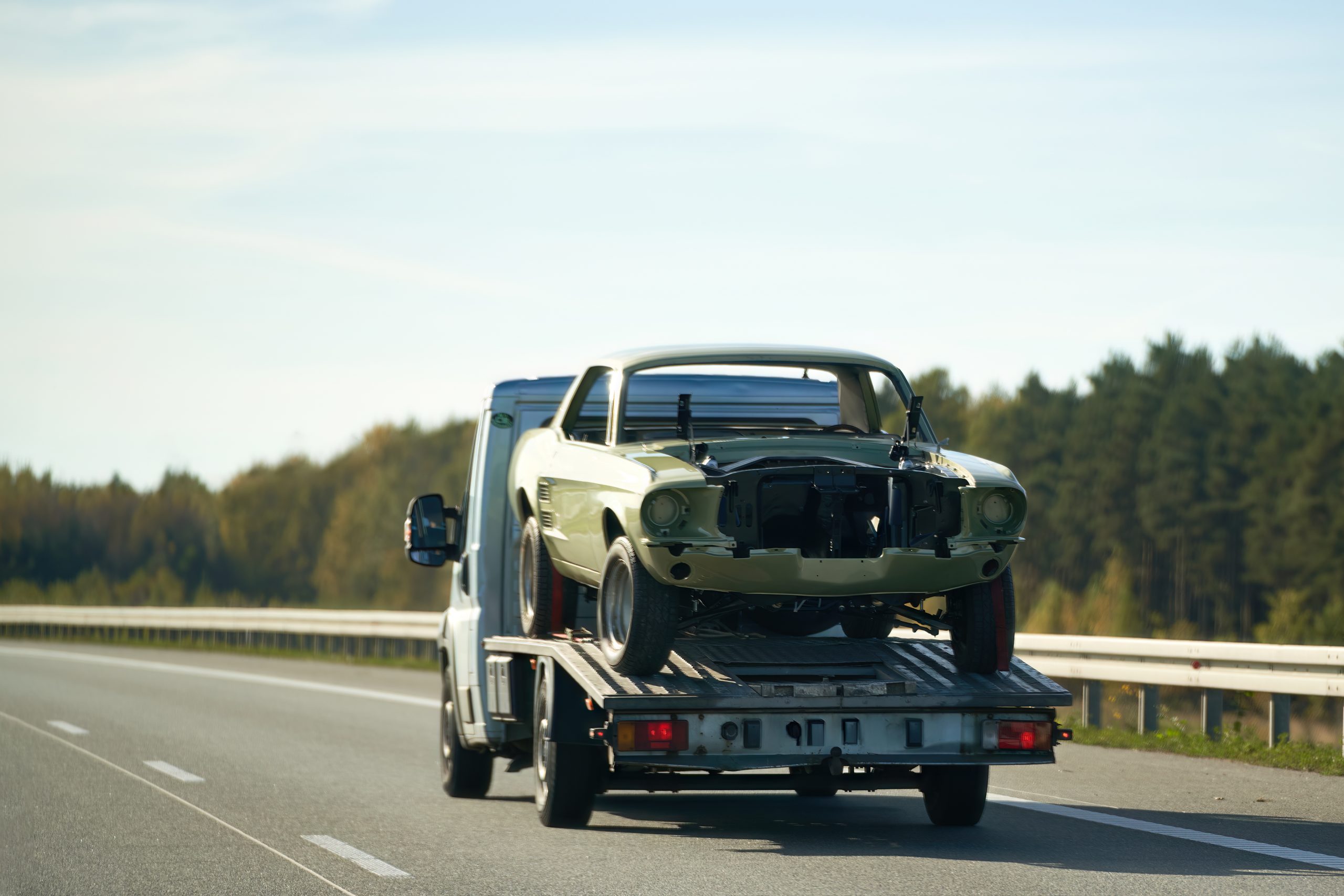 Flatbed tow truck carrying a classic car shell on a highway in Southern California, showing safe vehicle transport by Foglesong Towing.